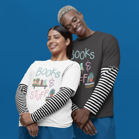 Modeled product image of Moxie•Pop's unisex graphic tee with "Books & Stuff" with books and house plants artwork in dark grey heather and white. Models are in front of a blue backdrop, wearing blue shorts, and a striped long sleeve underneath the graphic tee.