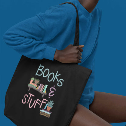 Product image of Moxie•Pop's eco tote bag with "Books & Stuff" with books and house plants artwork in black with sitting model holding the tote. 