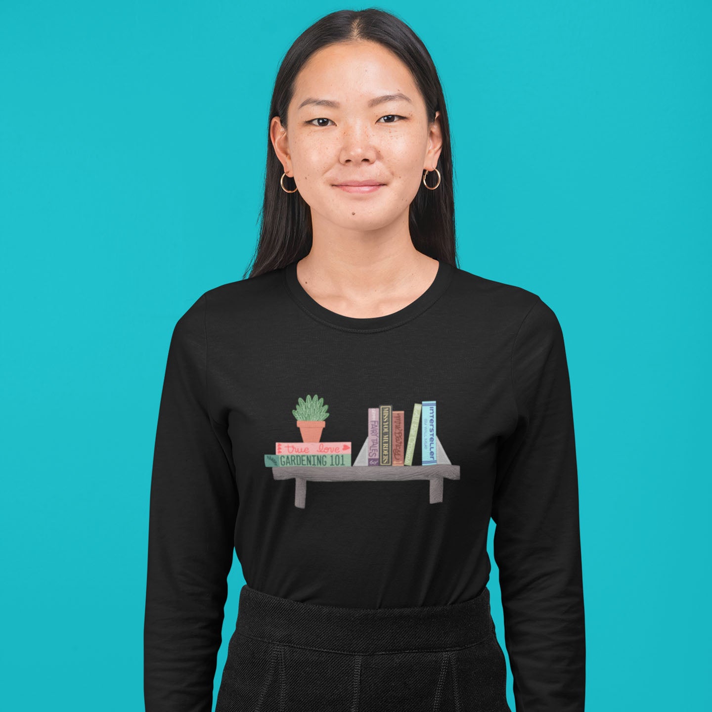 Modeled product image of Moxie•Pop's men's long sleeve graphic tee with a illustration of a shelf, a series of books atop, and a house plant in black