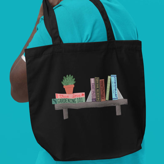 Product image of Moxie•Pop's eco tote bag with a hand drawn bookshelf containing books and a houseplant in black being modeled, thrown over the shoulder of a male in turquoise. 