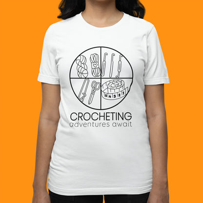 Modeled product image of Moxie•Pop's unisex graphic tee with "CROCHETING adventures await" below a circle filled with crocheting implements icons design in white