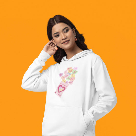 Moxie•Pop's unisex graphic hoodie with Valentine's conversation hearts with quotes from the Friends TV show and a box that reads "Friends Love" in white being modeled by a woman with an orange backdrop.