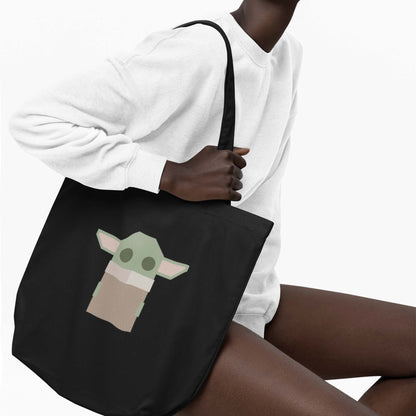 Moxie•Pop's eco tote bag with a geometric-styled Grogu in black modeled by a woman sitting wearing a white sweatshirt with a white backdrop.