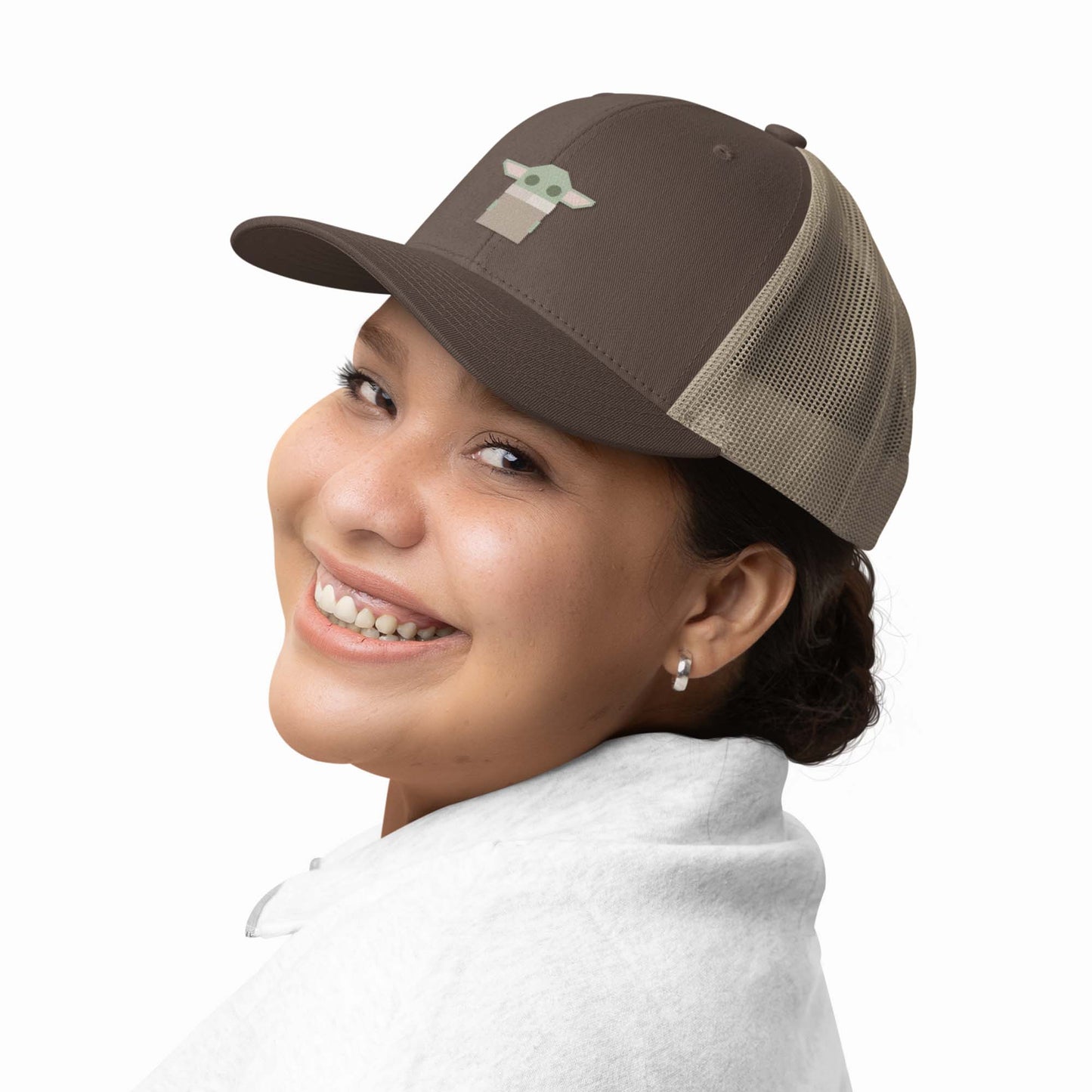 Moxie•Pop's embroidered trucker hat with a geometric-style Grogu in brown with khaki modeled by a woman in a bun with a white sweater and a white backdrop. 