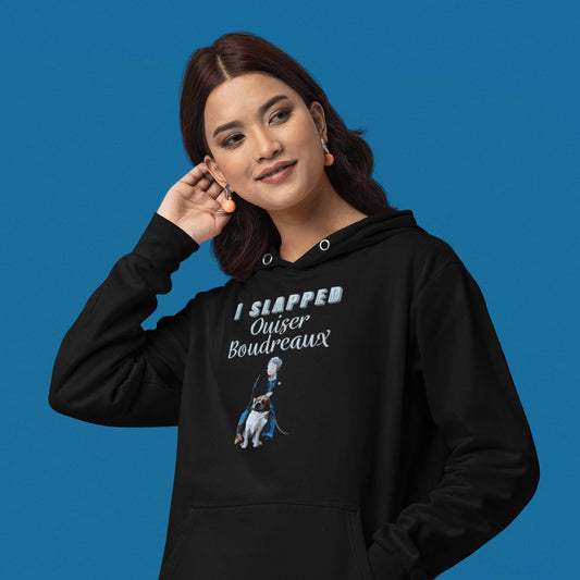 Moxie•Pop's unisex graphic hoodie with the hand lettered phrase "I slapped Ouiser Boudreaux" and and illustration of Ouiser and her St. Bernard, Rex design in black modeled by a woman with long hair and a blue backdrop