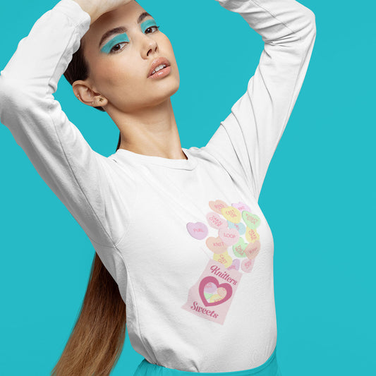 Modeled product image of Moxie•Pop's men's long sleeve graphic tee with a box of "Knitter Sweets" and Valentine's conversation hearts with knitting terms design in white