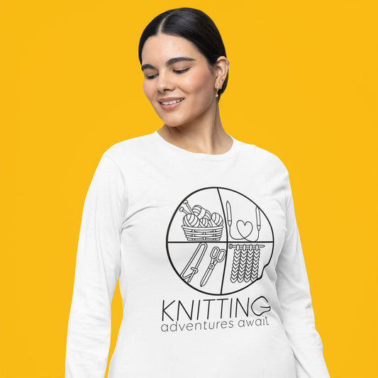 Modeled product image of Moxie•Pop's men's long sleeve graphic tee with "KNITTING adventures await" below a circle filled with knitting implements icons design in white