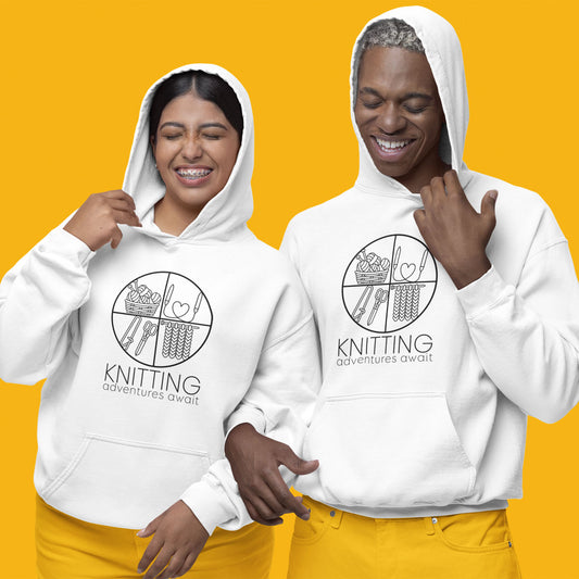 Modeled product image of Moxie•Pop's unisex graphic hoodie with "KNITTING adventures await" below a circle filled with knitting implements icons design in white. Models are wearing yellow pants standing in front of a yellow background."