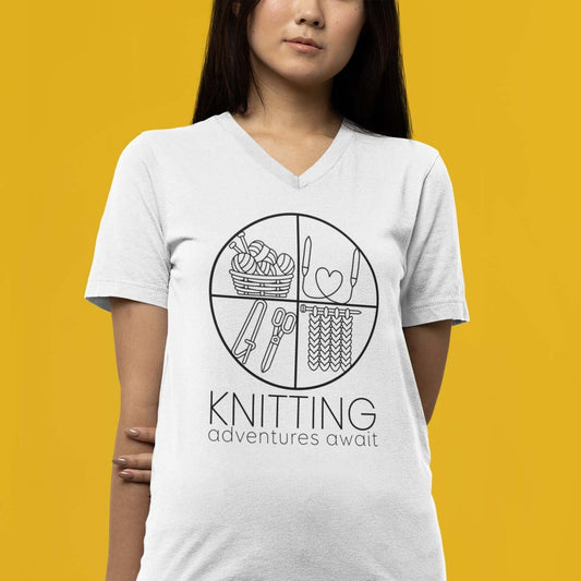 Moxie•Pop's unisex v-neck graphic tee with "KNITTING adventures await" below a circle filled with knitting implements icons design in white modeled by a woman with long hair and a yellow backdrop. 