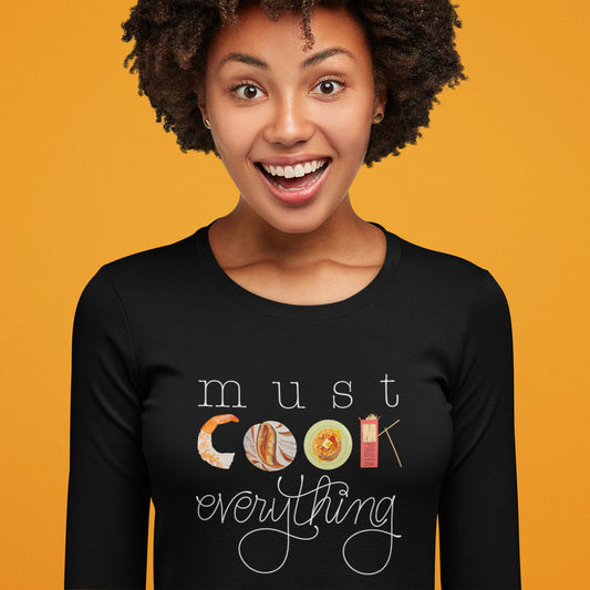 Modeled product image of Moxie•Pop's men's long sleeve graphic tee with "must COOK everything" with the word cook created from hand drawn food in black. 