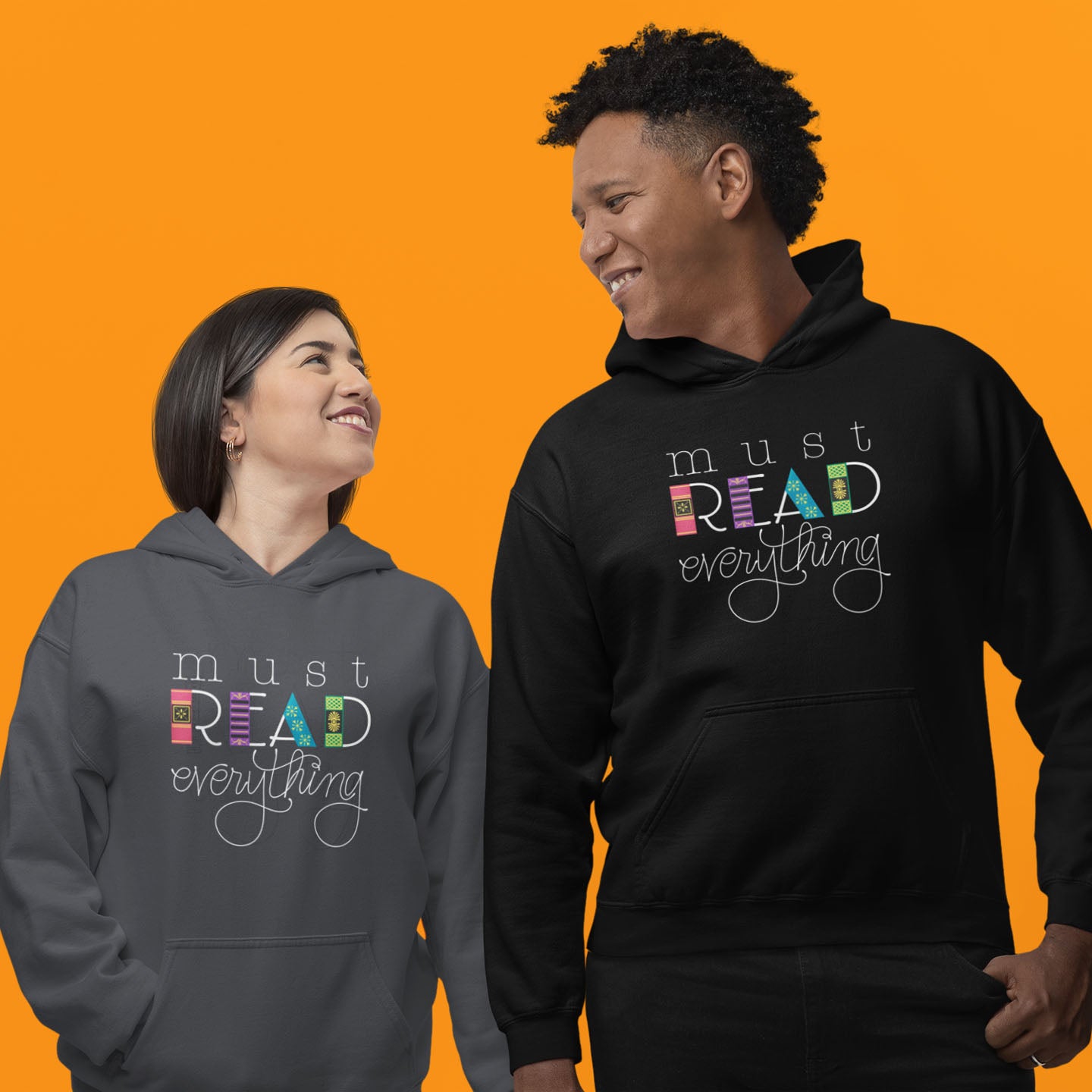 Modeled product image of Moxie•Pop's unisex graphic hoodie with 'Must Read Everything' with the downstroke of the word READ is created with hand drawn book spines in black and dark grey