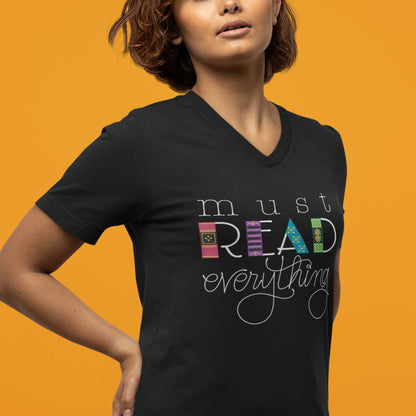 Moxie•Pop's unisex v-neck tee with hand lettered "Must Read Everything" with the downstrokes of the word 'READ' are hand drawn book spines in black modeled by a woman with short hair. 