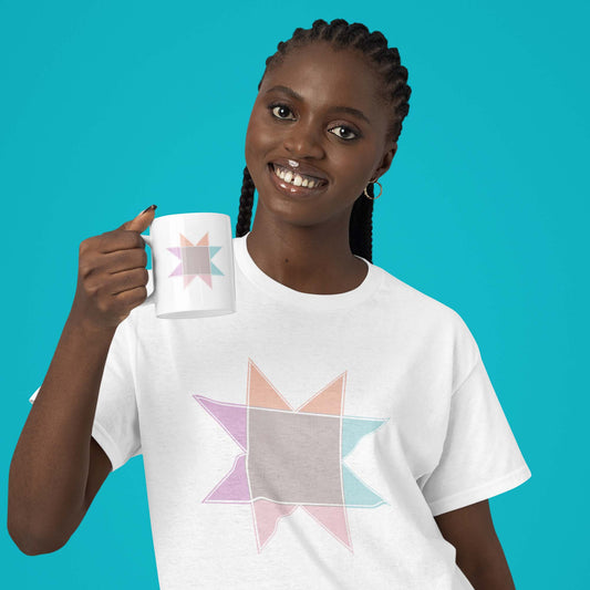 Moxie•Pop's white ceramic mug with a Pastel Quilt Block being held by a woman with long braids wearing a pastel quilt block tee in white with a turquoise backdrop.