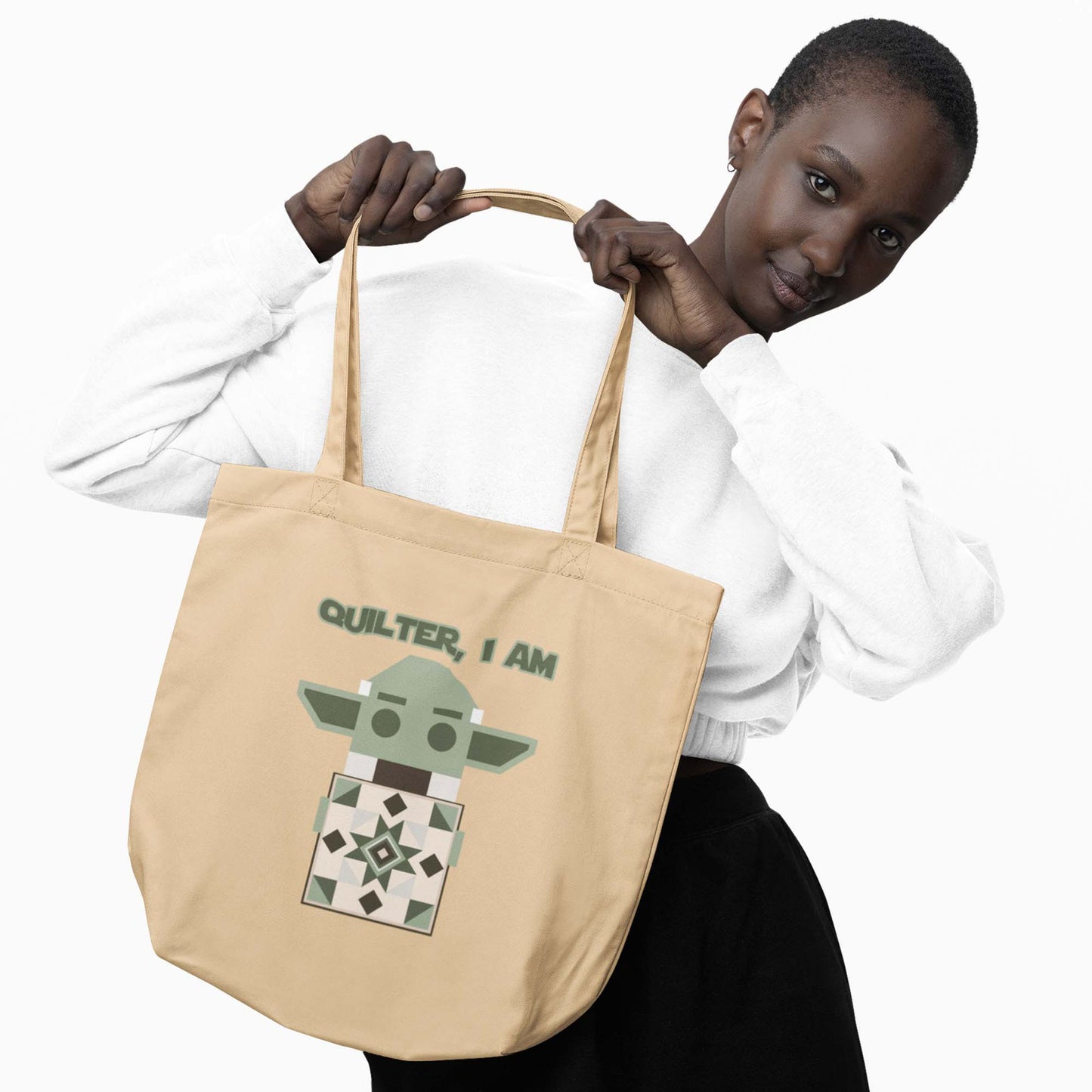 Moxie•Pop's eco tote bag with a geometric Yoda holding a quilt with the phrase "Quilter, I am" design in oyster being modeled by a woman in short hair. 