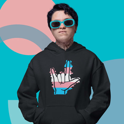 Moxie•Pop's unisex graphic hoodie with blue, pink, and white stripes behind a black ASL I love you hand sign icon in support of transgendered design in black modeled by a man with turquoise sunglasses and turquoise backdrop