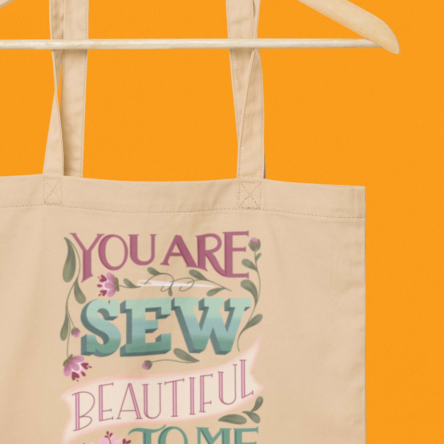 Hanging product image of Moxie•Pop's eco tote bag with "You are Sew Beautiful to me" in lavender with flowers in black with an orange backdrop. 