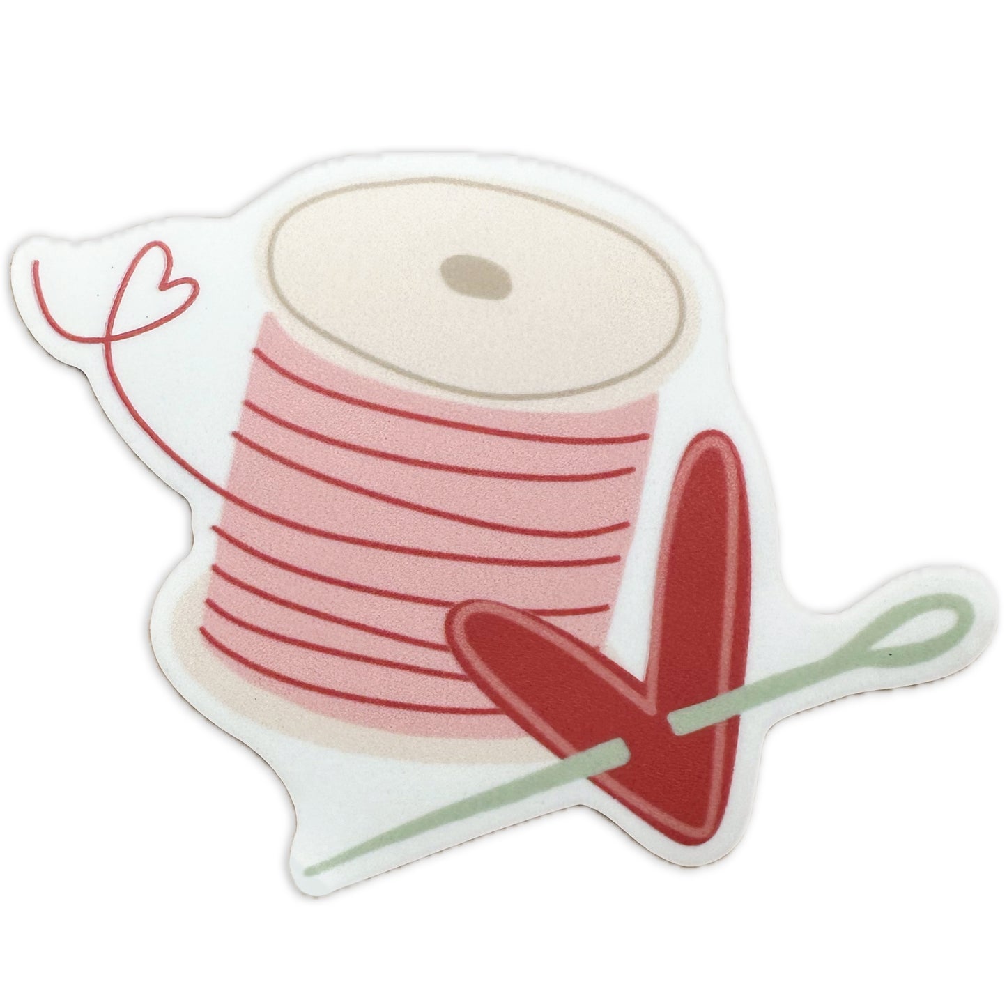 Lay flat product image of Moxie•Pop's water proof vinyl sticker with a hand-drawn spool of pink thread and a heart with a needle piercing it. 