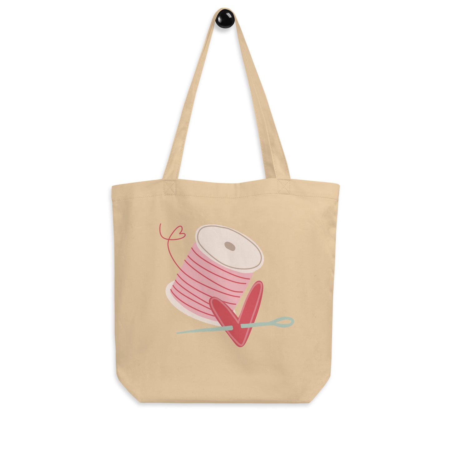 Moxie•Pop's eco tote bag in oyster with a spool of pink thread and a heart pierced by a needle hand-drawn design