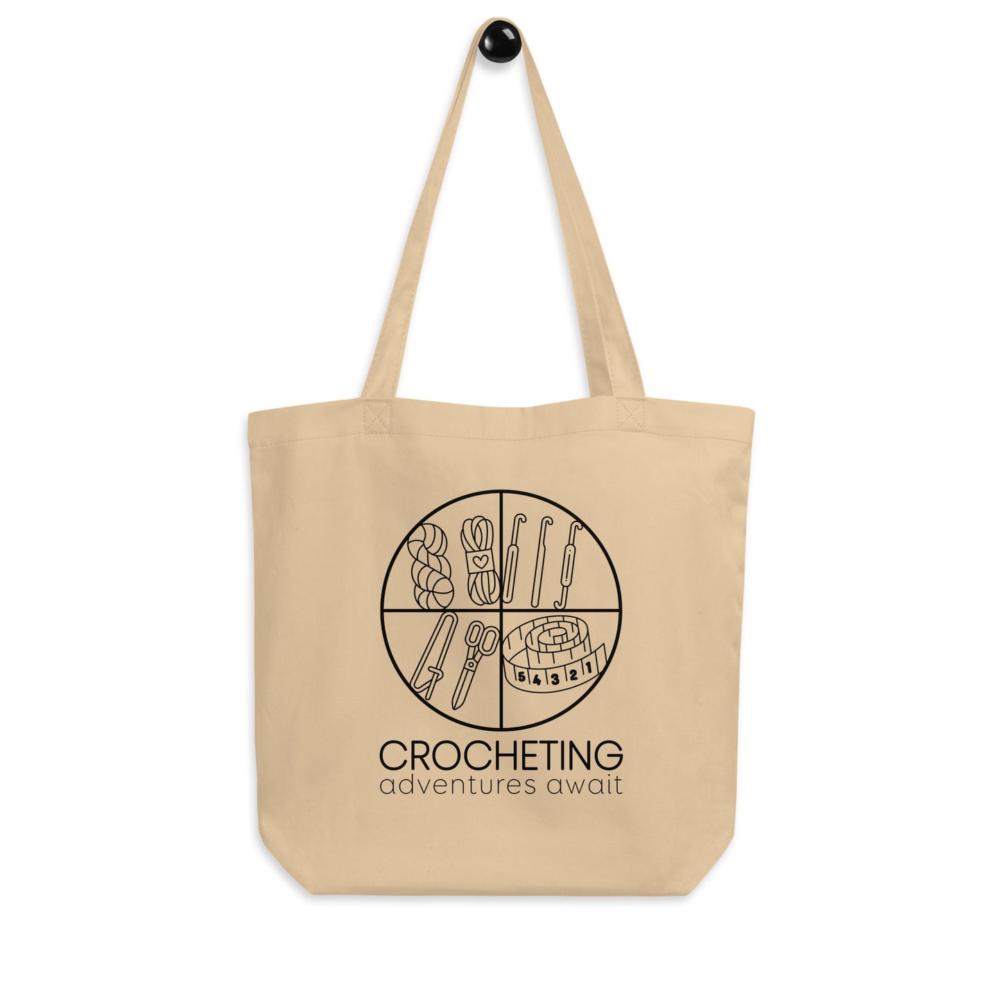 Hanging product image of Moxie•Pop's eco tote bag with "CROCHETING adventures await" below a circle filled with crocheting implements icons design in oyster