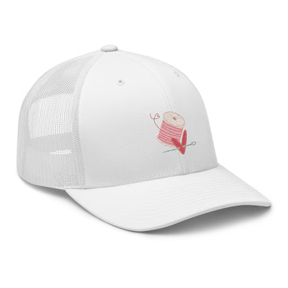 Moxie•Pop's retro trucker hat product image in white embroidered with pink spool of thread with a heart being pierced by a needle.