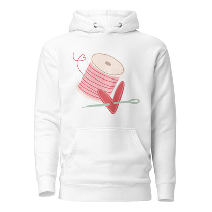 Moxie•Pop's unisex graphic hoodie in white with a spool of pink thread and a heart pierced by a needle hand-drawn design.