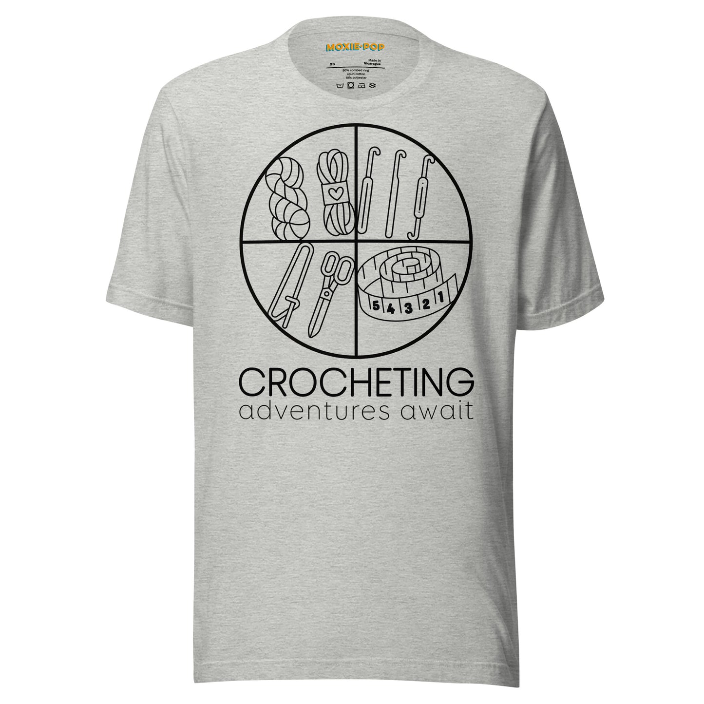 Ghost product image of Moxie•Pop's unisex graphic tee with "CROCHETING adventures await" below a circle filled with crocheting implements icons design in athletic heather