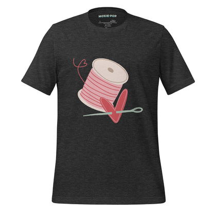 Ghost product image of Moxie•Pop's unisex graphic tee with a hand drawn spool of pink thread and a heart pierced by a needle in dark grey heather