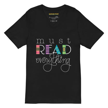 Lay flat product image of Moxie•Pop's unisex v-neck tee with hand lettered "Must Read Everything" with the downstrokes of the word 'READ' are hand drawn book spines in black. 