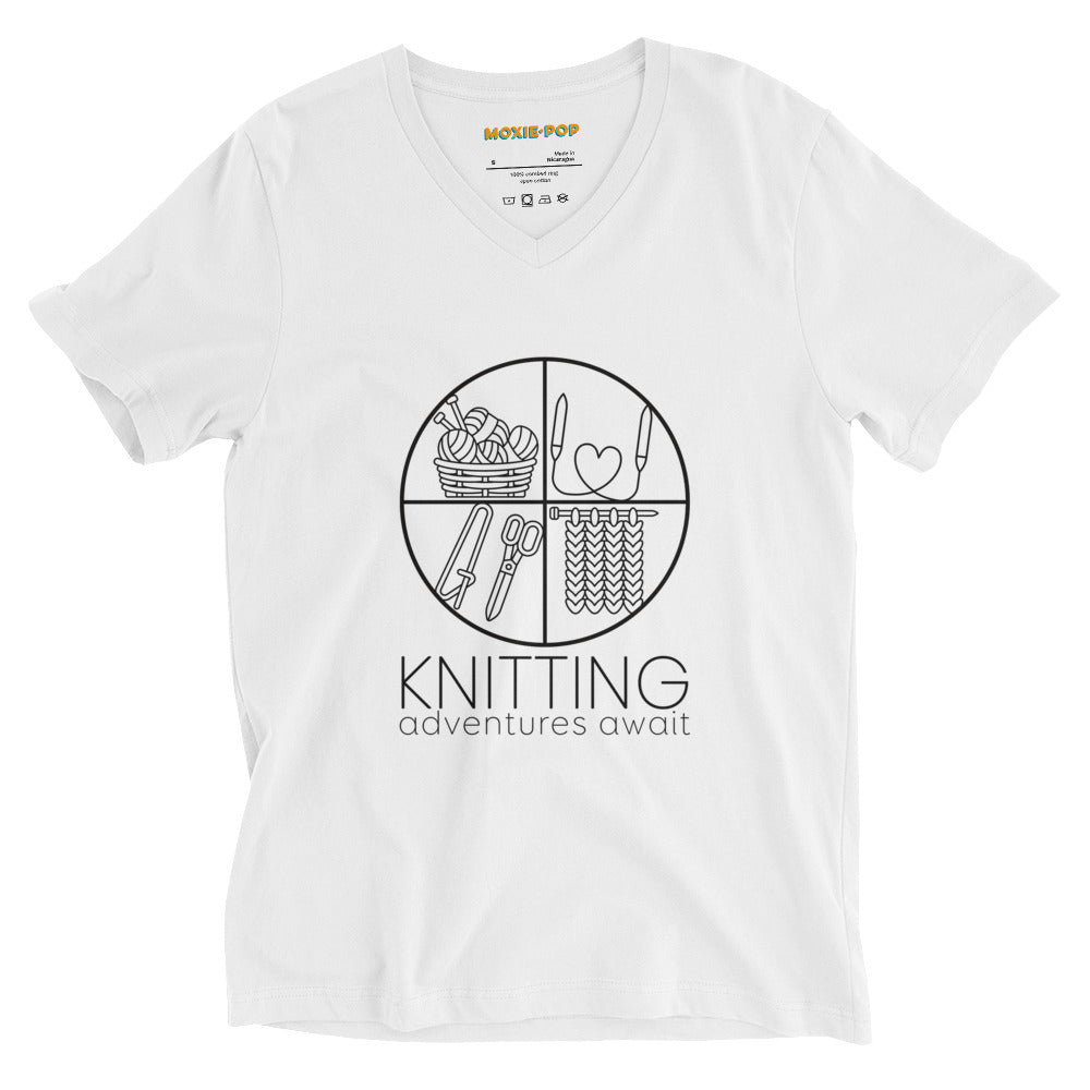 Lay flat product image of Moxie•Pop's unisex v-neck graphic tee with "KNITTING adventures await" below a circle filled with knitting implements icons design in white